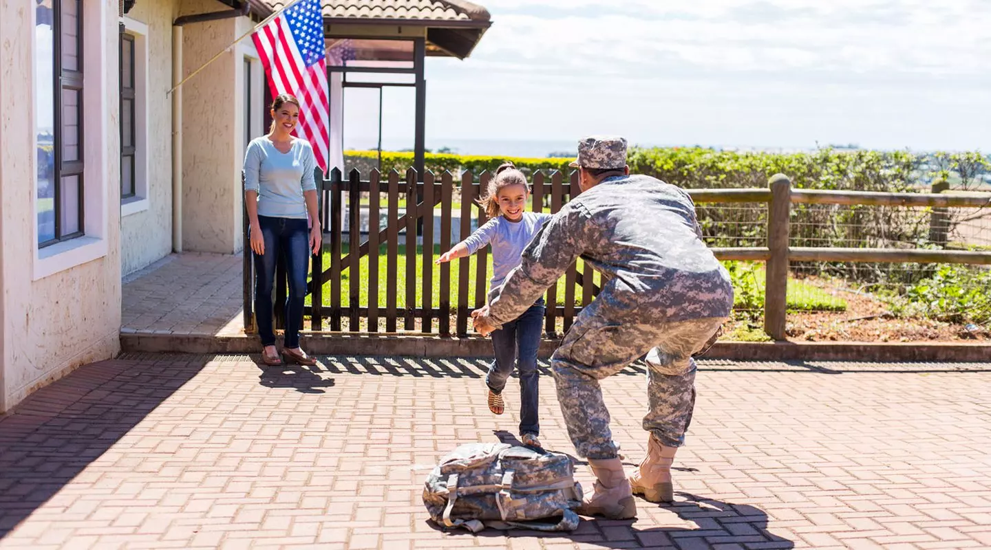 Soldier hugging daughter in front of house