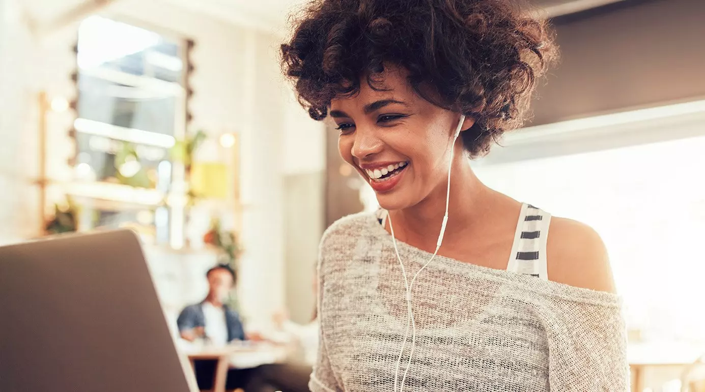 Black woman smiling listening to music on her laptop