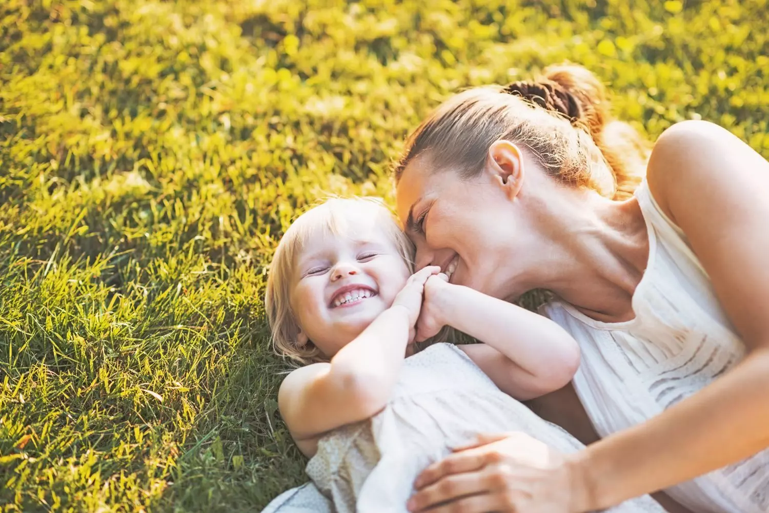 Mom snuggling her daughter outside laying on grass