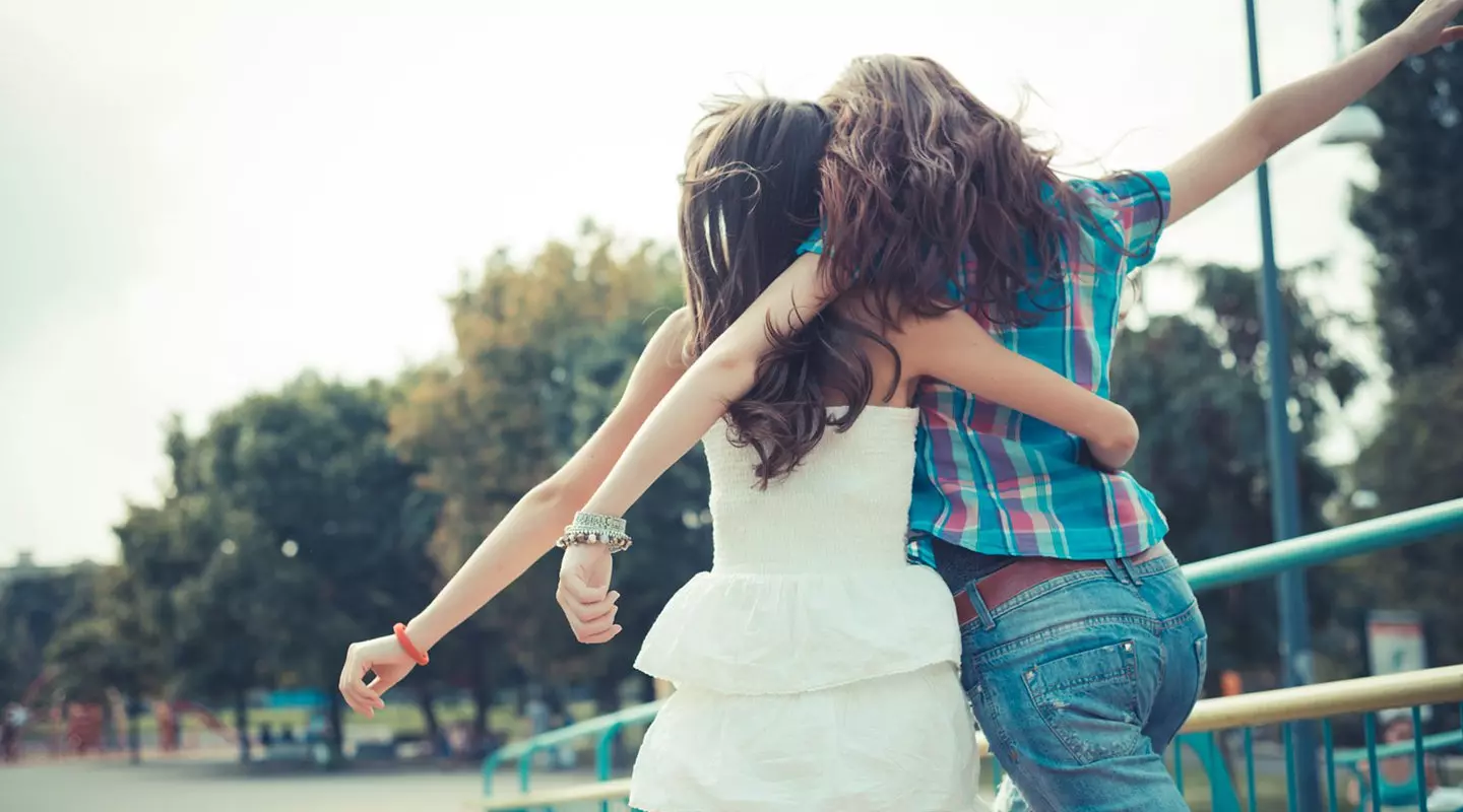 2 girls with their arms around each other facing away