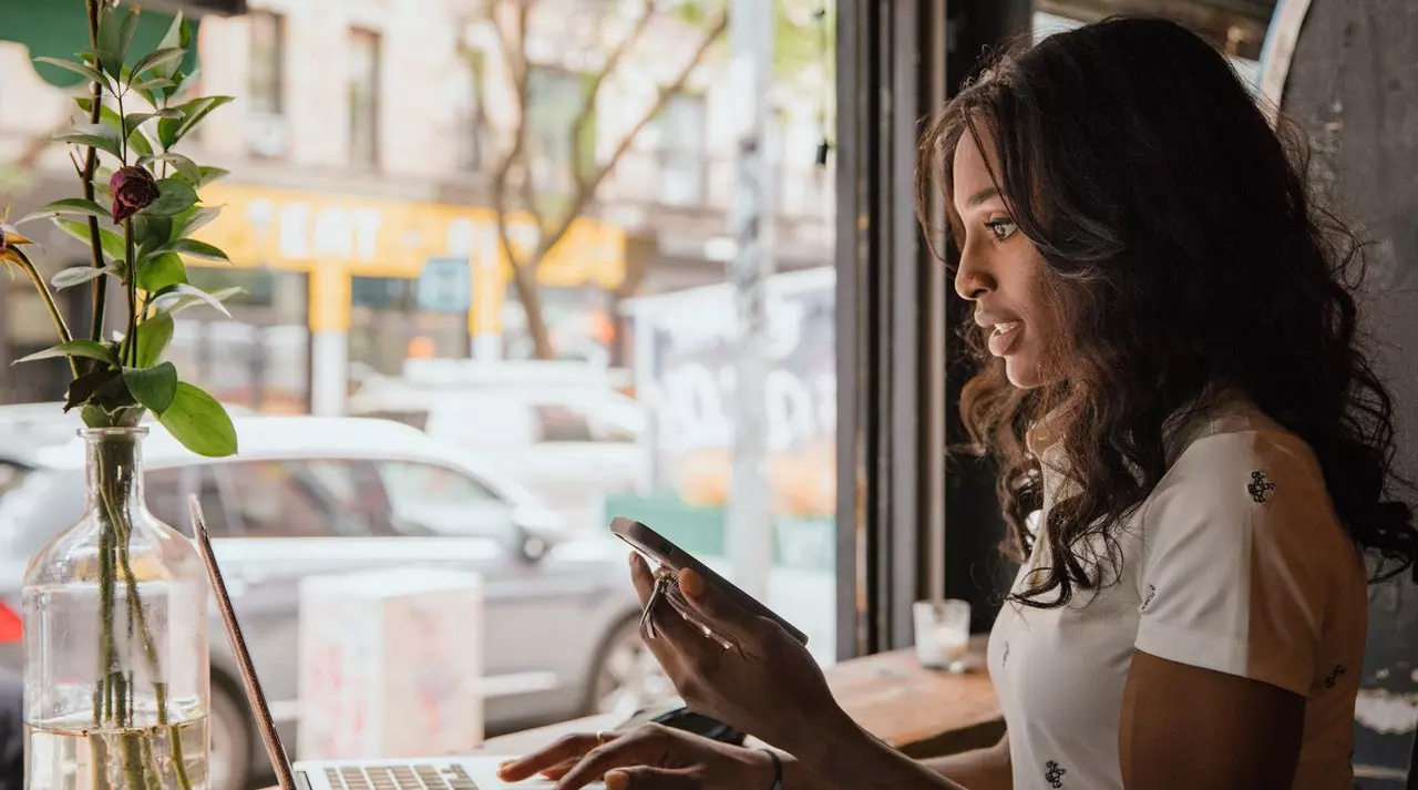 woman holding phone searching on laptop