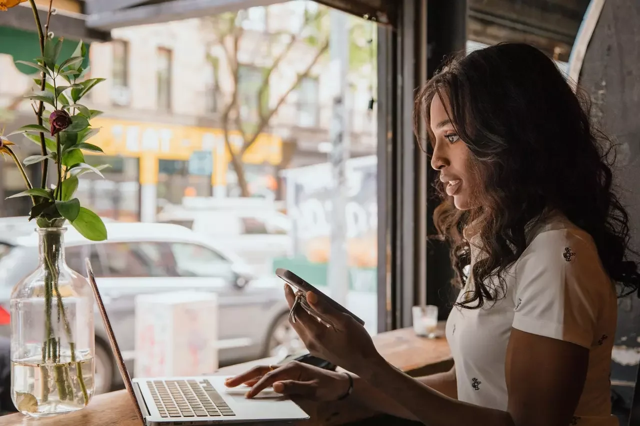 woman holding phone searching on laptop